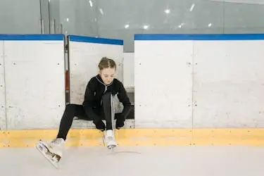 Child sitting on an ice rink tying ice skates.
