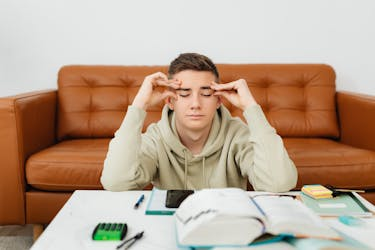 Teenager holding his head with stressed expression in front of his books